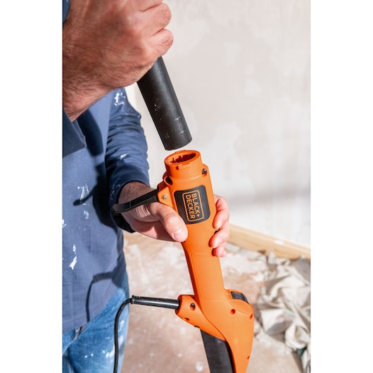 Persoon monteert een BLACK+DECKER oranje gereedschap met zwarte opzetstuk voor bouw of renovatie.