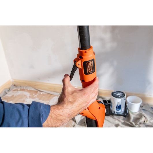 Hand stelt BLACK+DECKER polesander af in kamer met verfblikken op de vloer.
