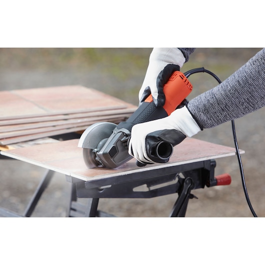 BLACKDECKER BEG220A1 haakse slijper in gebruik bij het snijden van tegels, close-up van handen met gereedschap.