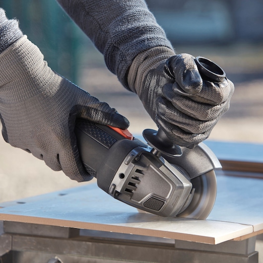 BLACKDECKER BEG220KA5 haakse slijper snijdt tegel, close-up van gehandschoende handen met gereedschap.