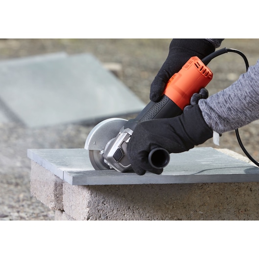 BLACK+DECKER BEG220K haakse slijper in gebruik voor het snijden van een tegel, close-up met handschoenen.