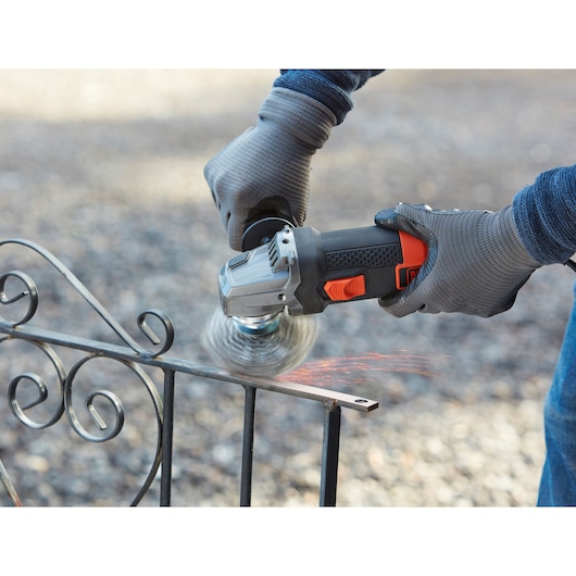 BLACKDECKER BEG220K haakse slijper gebruikt op metalen hek, close-up met vonken en handschoenen.