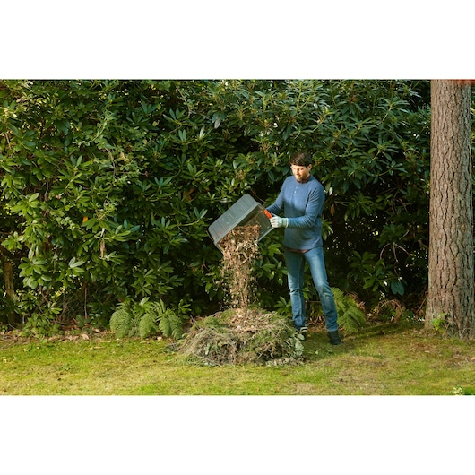 BLACKDECKER BEGAS5800 tuinhakselaar, persoon stort versnipperd materiaal op een composthoop buiten.