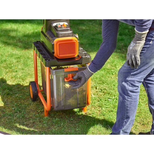 Foto van BLACKDECKER BEGAS5800 tuinhakselaar met doorzichtige opvangbak, persoon met handschoenen aan het handvat buiten.