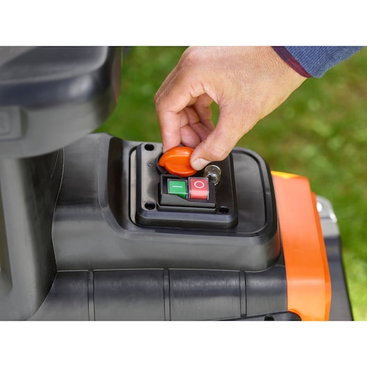 Close-up van BLACKDECKER BEGAS5800 bedieningspaneel met hand aan oranje veiligheidsknop, groene en rode aan/uit-knoppen zichtbaar.