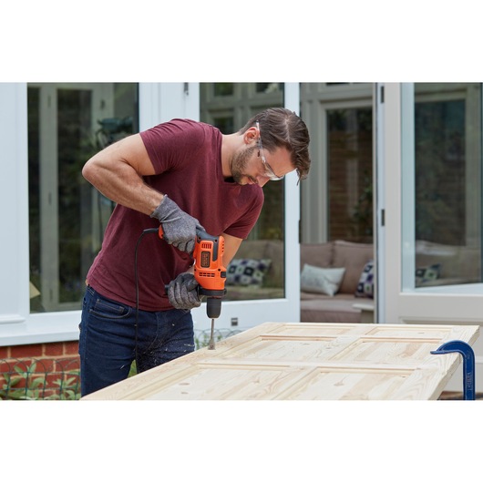 BLACKDECKER BEH200K perceuse filaire utilisée sur une porte en bois, avec des gants, en extérieur.