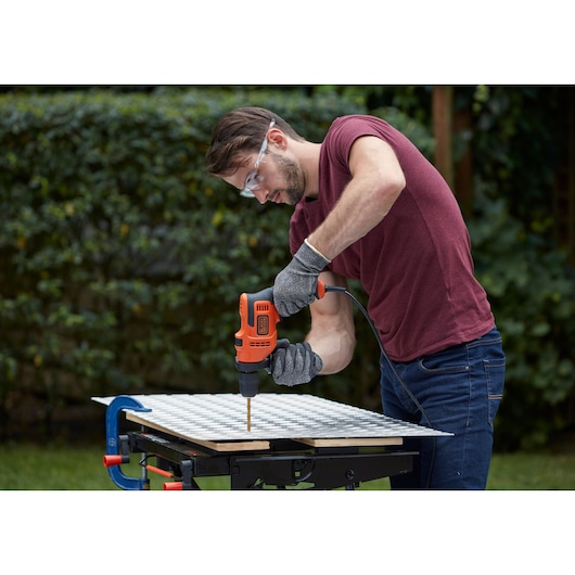 Perceuse filaire BLACKDECKER BEH200K pour le travail du bois en extérieur, gants et lunettes de protection.