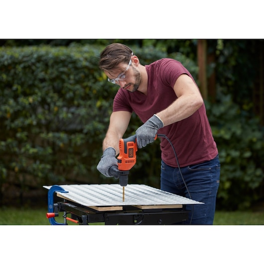 Photo d'une personne utilisant une perceuse filaire BLACKDECKER BEH200 sur un établi en extérieur, perçant une tôle.