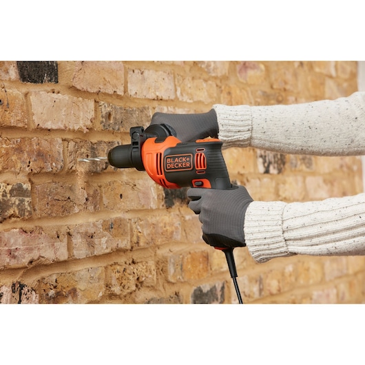 Photo de la perceuse à percussion BLACK+DECKER BEH550 en action, perçant un mur en briques.