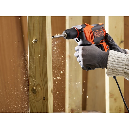 BLACK+DECKER BEH710K perceuse filaire en action, perçant du bois, gros plan sur une main gantée.