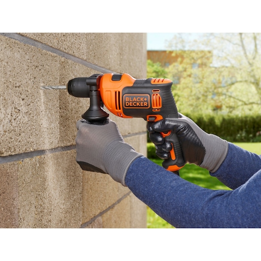 Perceuse sans fil orange BLACKDECKER BEH710K utilisée sur mur en béton en extérieur, vue rapprochée.
