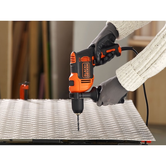 Perceuse filaire BLACK+DECKER BEH710SA32 utilisée sur une plaque métallique, utilisateur avec gants et pull.