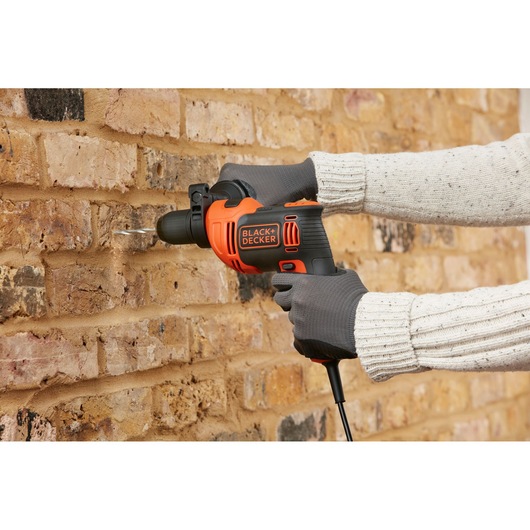 BLACK+DECKER BEH710 elektrische klopboormachine in gebruik bij het boren in een bakstenen muur, zwart-oranje ontwerp.