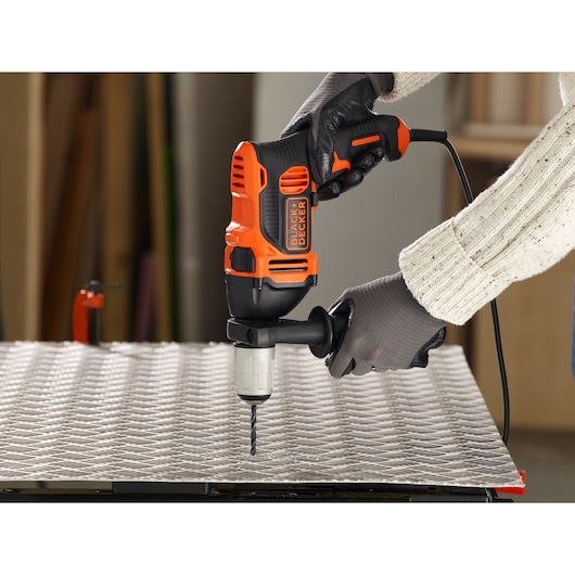 BLACKDECKER BEH850K perceuse à percussion filaire utilisée sur tôle par des mains gantées, vue rapprochée.