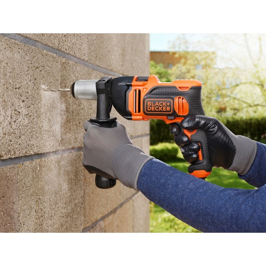 BLACK+DECKER BEH850 marteau perforateur orange et noir utilisé sur un mur en béton extérieur.
