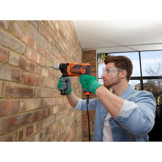 Photo de la perceuse filaire BLACKDECKER BEH850 utilisée sur un mur en briques, personne avec des gants verts.
