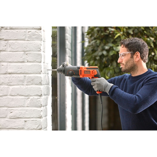 BLACKDECKER BEHS01K marteau perforateur filaire utilisé sur mur de briques blanches, design orange et noir, vue latérale.