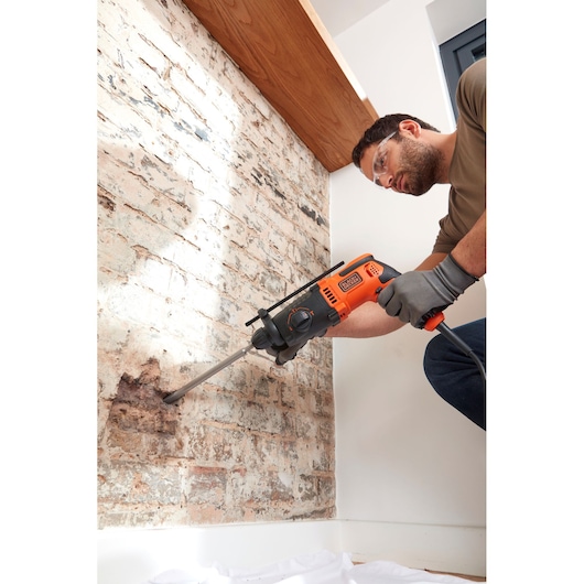 BLACKDECKER BEHS01K perforateur en action sur mur de briques, outil orange et noir, vue latérale.