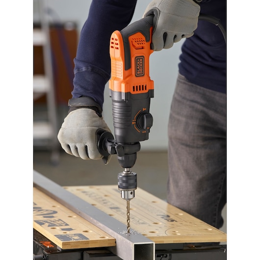 BLACKDECKER BEHS01 perceuse à percussion utilisée sur métal, corps orange et noir, utilisateur avec gants.