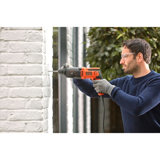 BLACKDECKER BEHS01 perceuse à percussion filaire utilisée sur un mur de briques blanches, photographie produit.