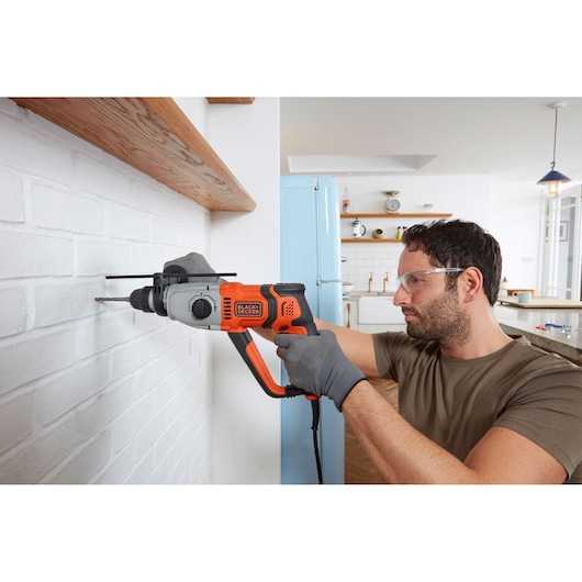 BLACKDECKER BEHS02K perceuse à percussion filaire utilisée sur un mur de briques blanches dans une cuisine.