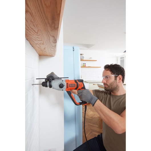 Photo de la perceuse à percussion BLACKDECKER BEHS02K utilisée sur un mur de briques blanches dans une cuisine moderne.