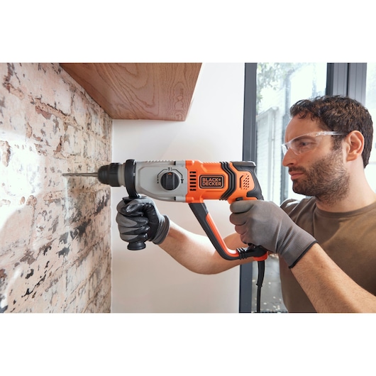 BLACK+DECKER BEHS02K marteau perforateur utilisé sur mur de briques, design orange et noir, personne avec des gants.