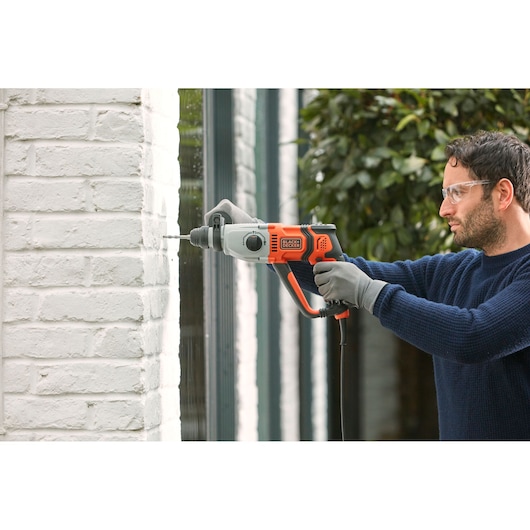 Photo de la perceuse à percussion BLACKDECKER BEHS02K utilisée pour percer un mur en briques blanches à l'extérieur.
