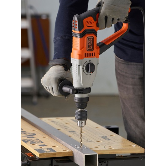 Perceuse à percussion BLACKDECKER BEHS02K utilisée pour percer du métal sur un établi, opérateur avec gants.