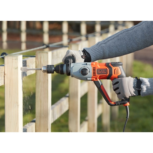 Photo de la perceuse à percussion filaire BLACKDECKER BEHS02K percant une barrière en bois dehors.