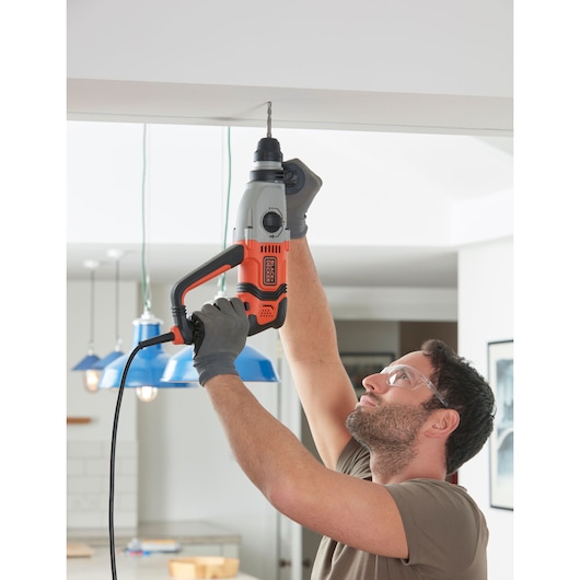 Photo de la perceuse à percussion filaire BLACKDECKER BEHS02K, utilisée par une personne sur un plafond intérieur.