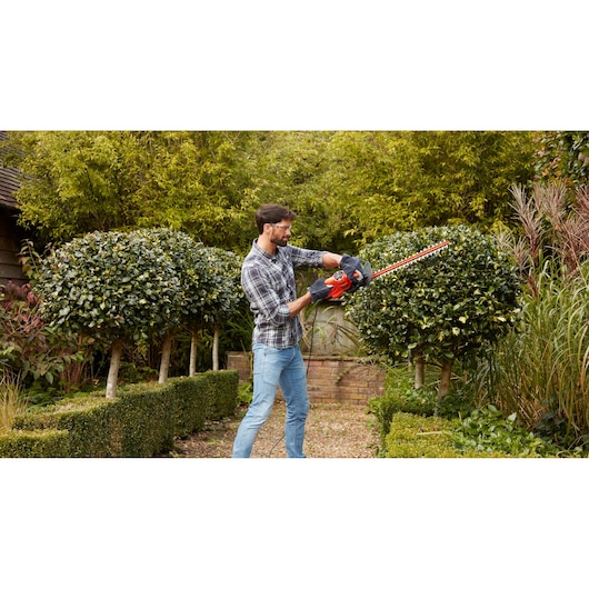 BLACKDECKER BEHT251KIT taille-haie utilisé dans un jardin, outil rouge et noir taillant des arbustes.