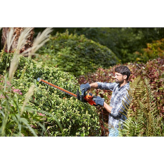 BLACKDECKER BEHTS401 heggenschaar gebruikt buiten voor het trimmen van dichte groene struiken.