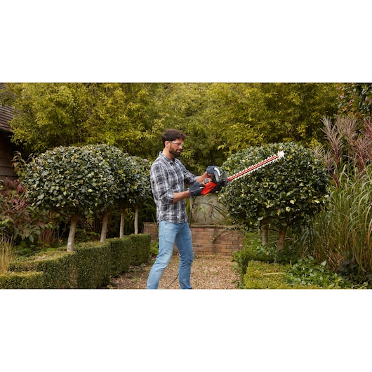 BLACKDECKER BEHTS401 heggenschaar in gebruik buiten, man trimt struiken in de tuin.