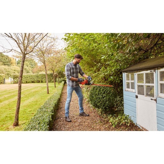 BLACKDECKER BEHTS401 heggenschaar gebruikt op tuinstruiken naast een blauwe schuur.