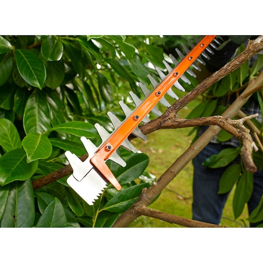 Dichtbij opname van BLACKDECKER BEHTS451 heggenschaarblad dat een dikke tak tussen groene bladeren knipt.