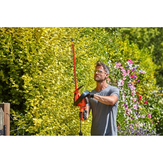 Foto van BLACKDECKER BEHTS551 heggenschaar in gebruik bij het trimmen van een hoge groene haag in de tuin.