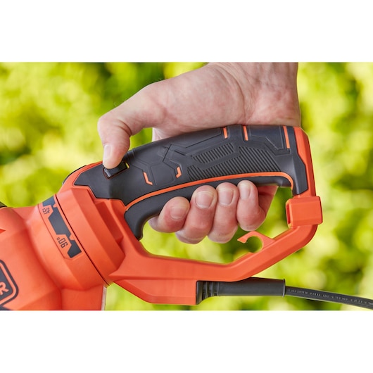 Close-up foto van het handvat van de BLACKDECKER BEHTS551 heggenschaar, vastgehouden door een hand, zwart met oranje details.