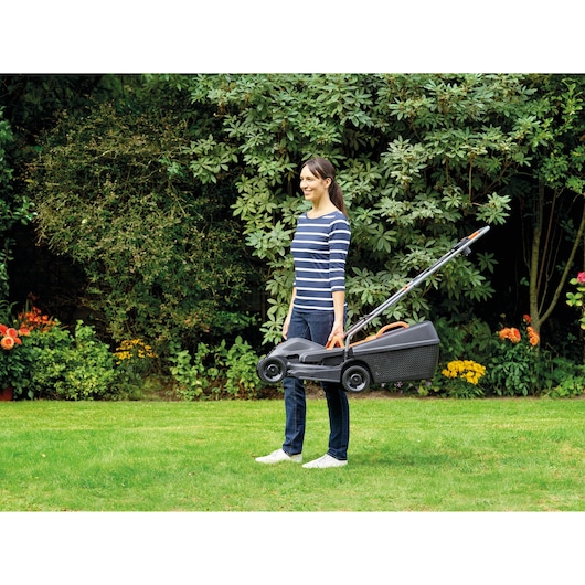 Photo d'une personne transportant la tondeuse BLACKDECKER BEMW351GL2 par la poignée dans un jardin.