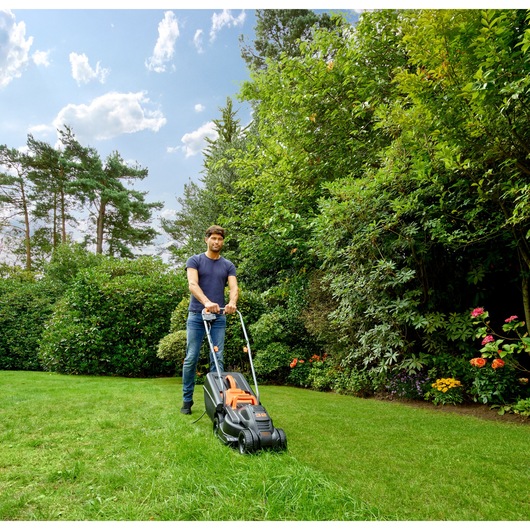 BLACKDECKER BEMW351 tondeuse utilisée à l'extérieur sur pelouse, fond de jardin, vue de côté.