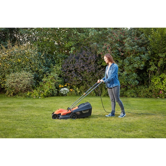 BLACKDECKER BEMW451 tondeuse électrique utilisée sur pelouse par une personne, orange et noir, vue latérale.