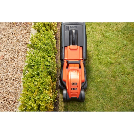 Tondeuse BLACK+DECKER BEMW451 vue de dessus tondant l’herbe au bord du jardin.