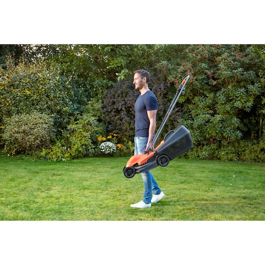 BLACKDECKER BEMW451 tondeuse portée par une personne dans un jardin avec pelouse et arbustes.