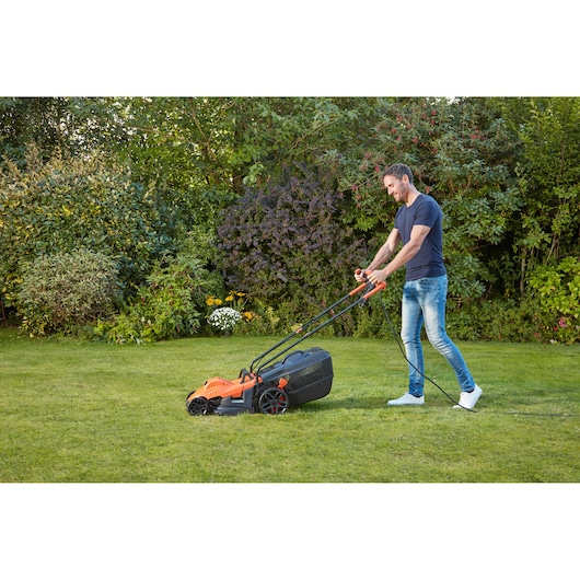 BLACKDECKER BEMW461BGL2 tondeuse utilisée sur pelouse, design orange et noir, cadre de jardin