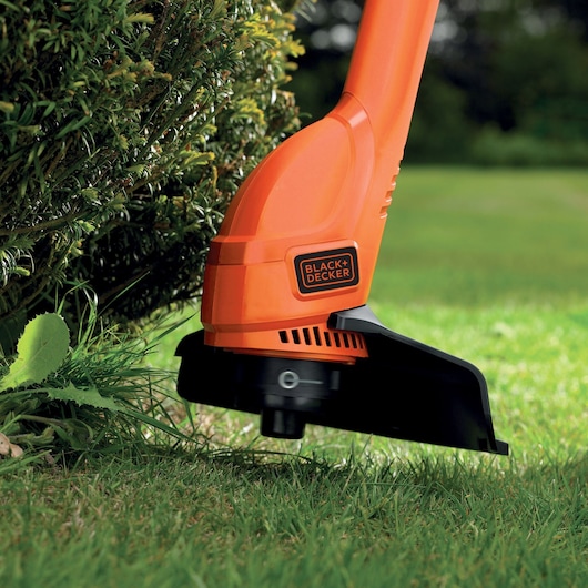 Photo du coupe-bordure orange BLACK+DECKER BEMW461BGL2 en action près des arbustes.