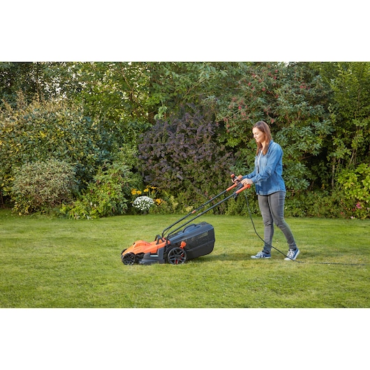 Personne utilisant la tondeuse électrique BLACKDECKER BEMW461BH sur une pelouse verte dans un jardin.