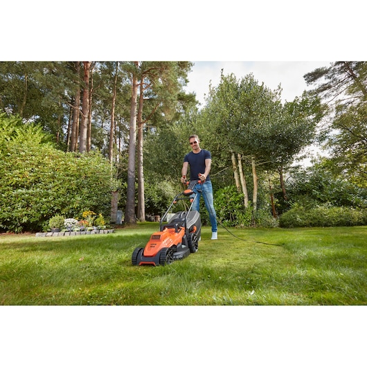 Foto van BLACKDECKER BEMW461ES elektrische grasmaaier in gebruik op gazon, oranje kleur, tuin op achtergrond.