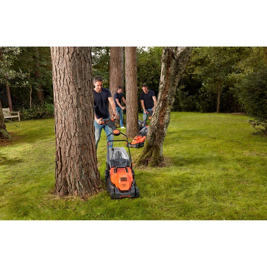BLACKDECKER BEMW461ES grasmaaier gebruikt door mensen om gras rond bomen in een tuin te maaien.