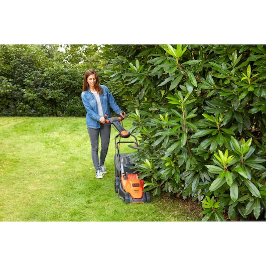 Foto van BLACKDECKER BEMW461ES grasmaaier in gebruik op gras naast struiken buiten.