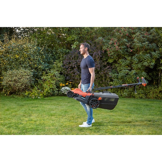 BLACKDECKER BEMW461ES grasmaaier gedragen door persoon in tuin, zijaanzicht.